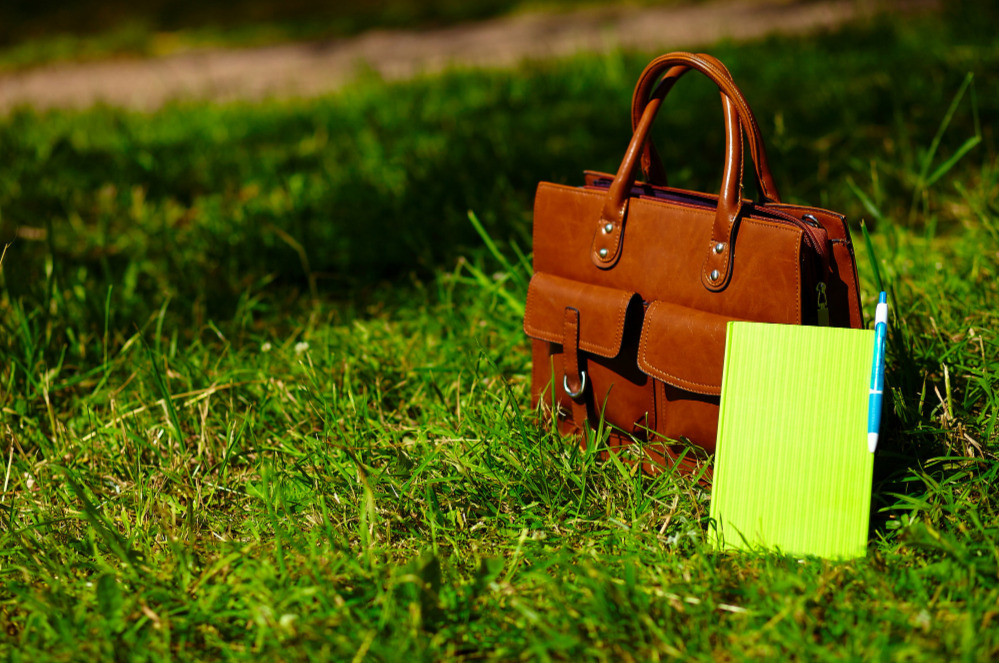 eco friendly travel tips illustrated by a handbag and notepad on green grass